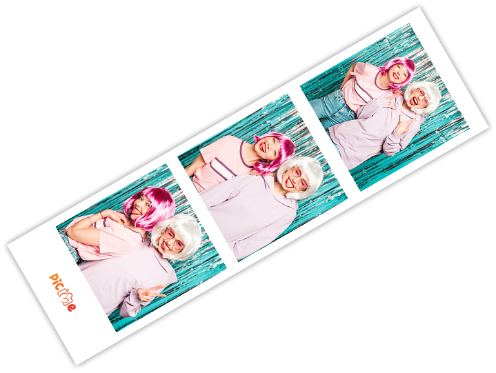 Fotobooth strip met vier sequentiële foto's van twee personen in roze kledij en pruiken liggend op turquoise houten ondergrond.