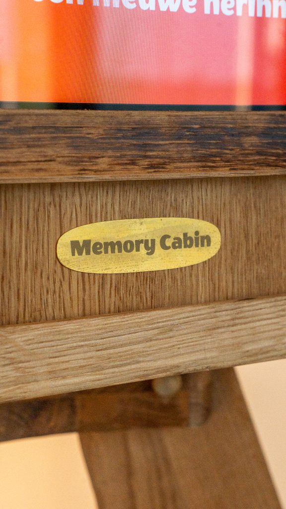 Geel ovaal typeplaatje met "Memory Cabin" tekst op houten meubel met gegroefde oppervlak.