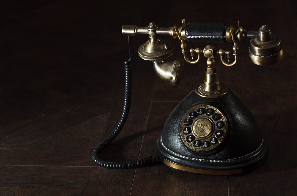 Vintage roterende telefoon met zwarte lederen voet, gouden details en draaischijf, met gouden hoorn bovenop op houten ondergrond.