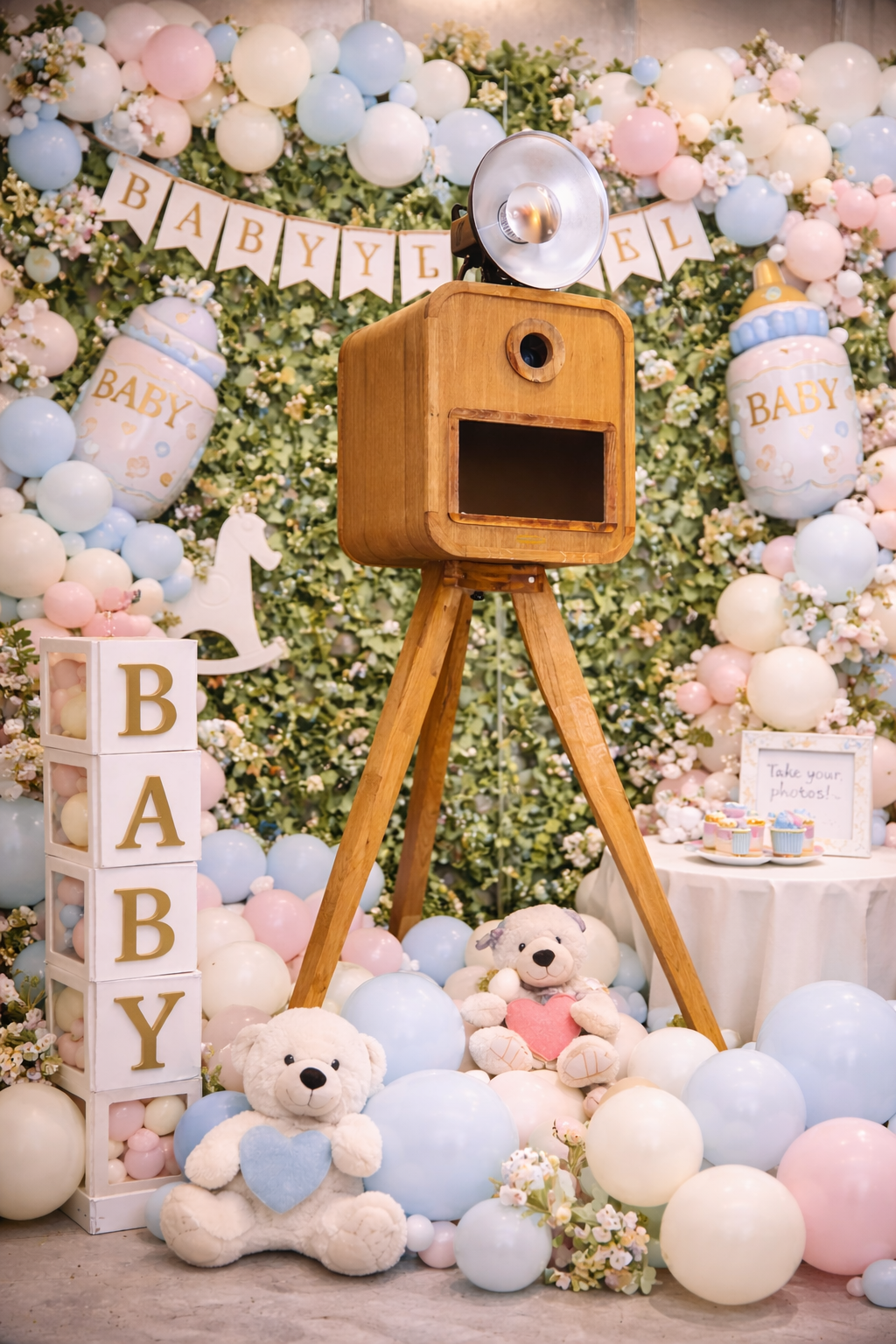 Houten fotocamera op statief met teddy bears en ballonnen voor een babyshower decoratie met bloemen en slingers.