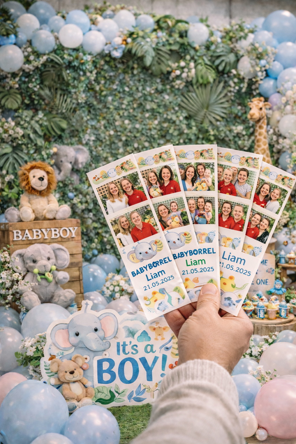 Hand houdt fotostrips vast met familiefoto's en "Babyborrel Liam 21.05.2025" voor een babyshower-decoratie met ballonnen, knuffels en bloemen.