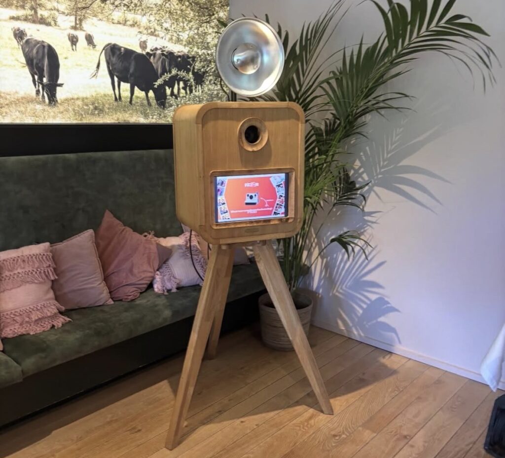 Houten MemoryCabin photobooth op driepoot met flitser, opgesteld in een woonruimte.