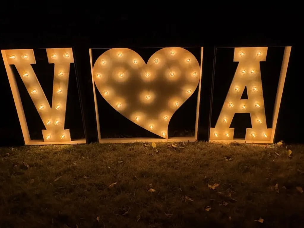 De lichtletters V, hart en A in een tuin, in het donker